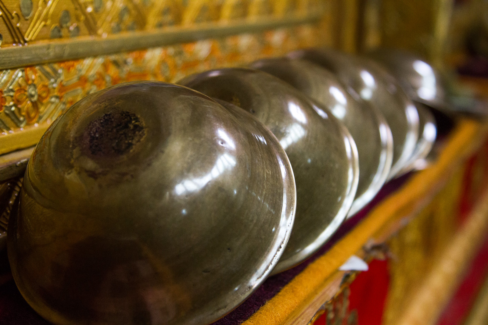 A row of polished silver offering bowls lined up against an ornate gilded temple wall.
