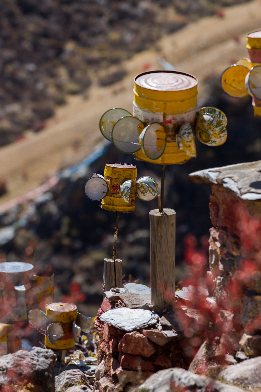 Weathered yellow tins and glass bowls mounted on wooden posts atop a stone wall in an arid mountain landscape