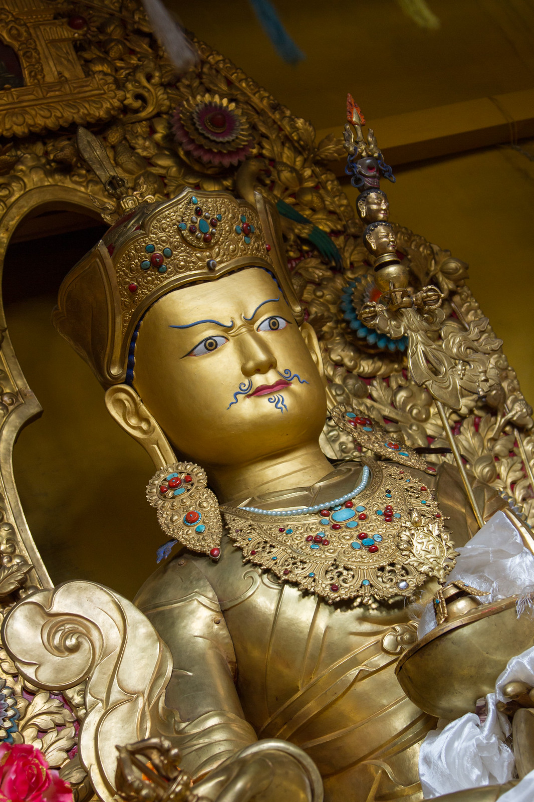 Ornate gilded Tibetan Buddhist statue with turquoise-and-coral jeweled crown and collar, holding a ritual scepter.