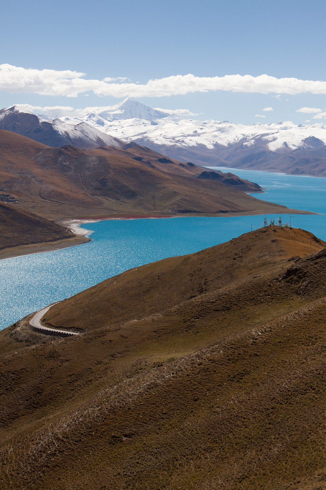 Turquoise Yamdrok Lake winding between barren brown hills below snow-capped Himalayan peaks in Tibet.