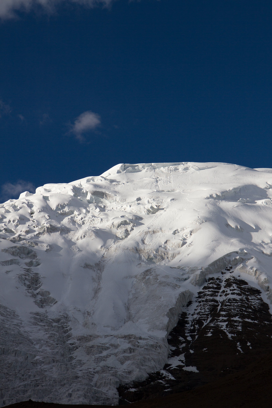 A snow-covered mountain summit with a glaciated face against a deep blue sky.