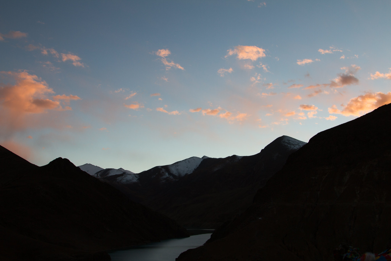 Snow-dusted Himalayan peaks and a river winding through silhouetted valleys under a pink-clouded dusk sky.