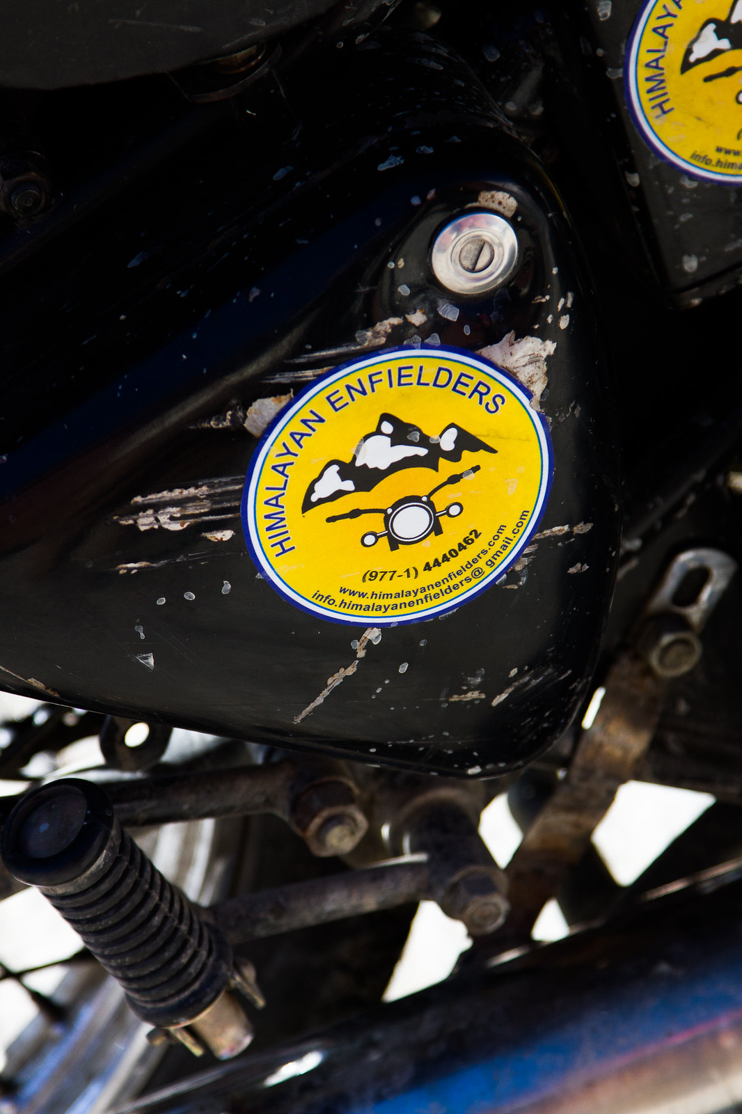 Weathered yellow "Himalayan Enfielders" sticker on the black engine casing of a Royal Enfield motorcycle