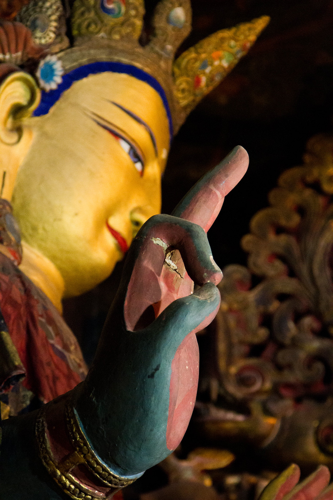 Gilded Tibetan Buddhist statue's serene face and jeweled crown, its blue-and-pink hand raised in a mudra.