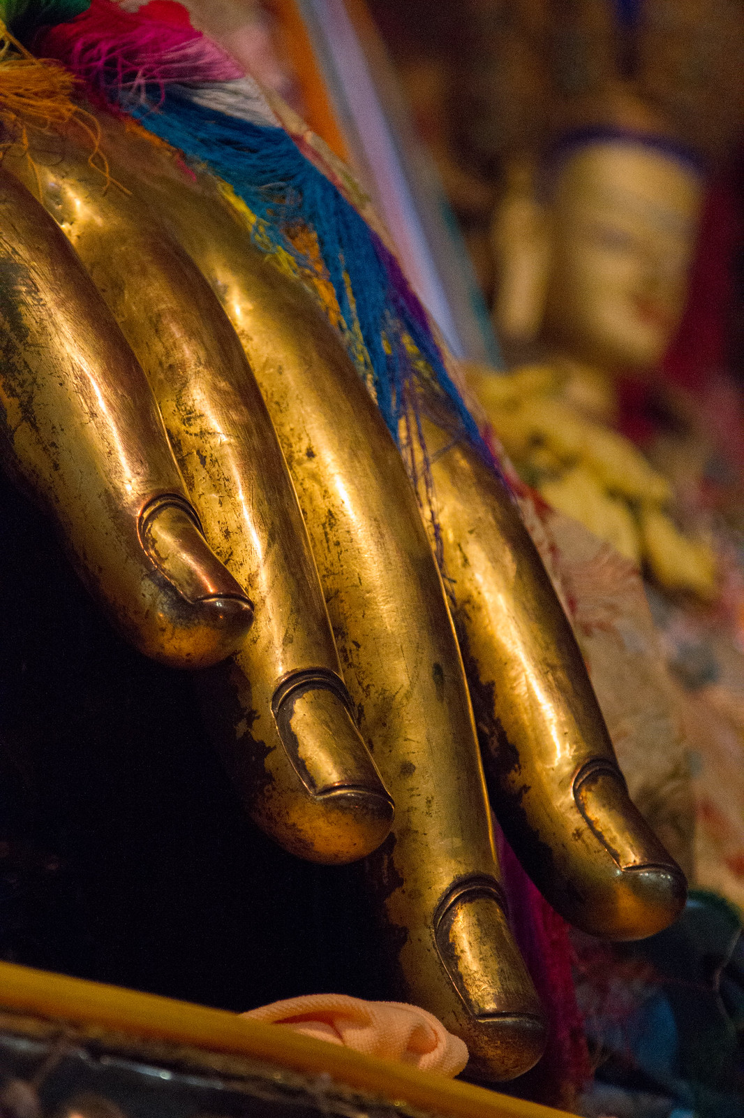 Close-up of a golden Buddha statue's hand draped with colorful silk offerings in a Tibetan temple