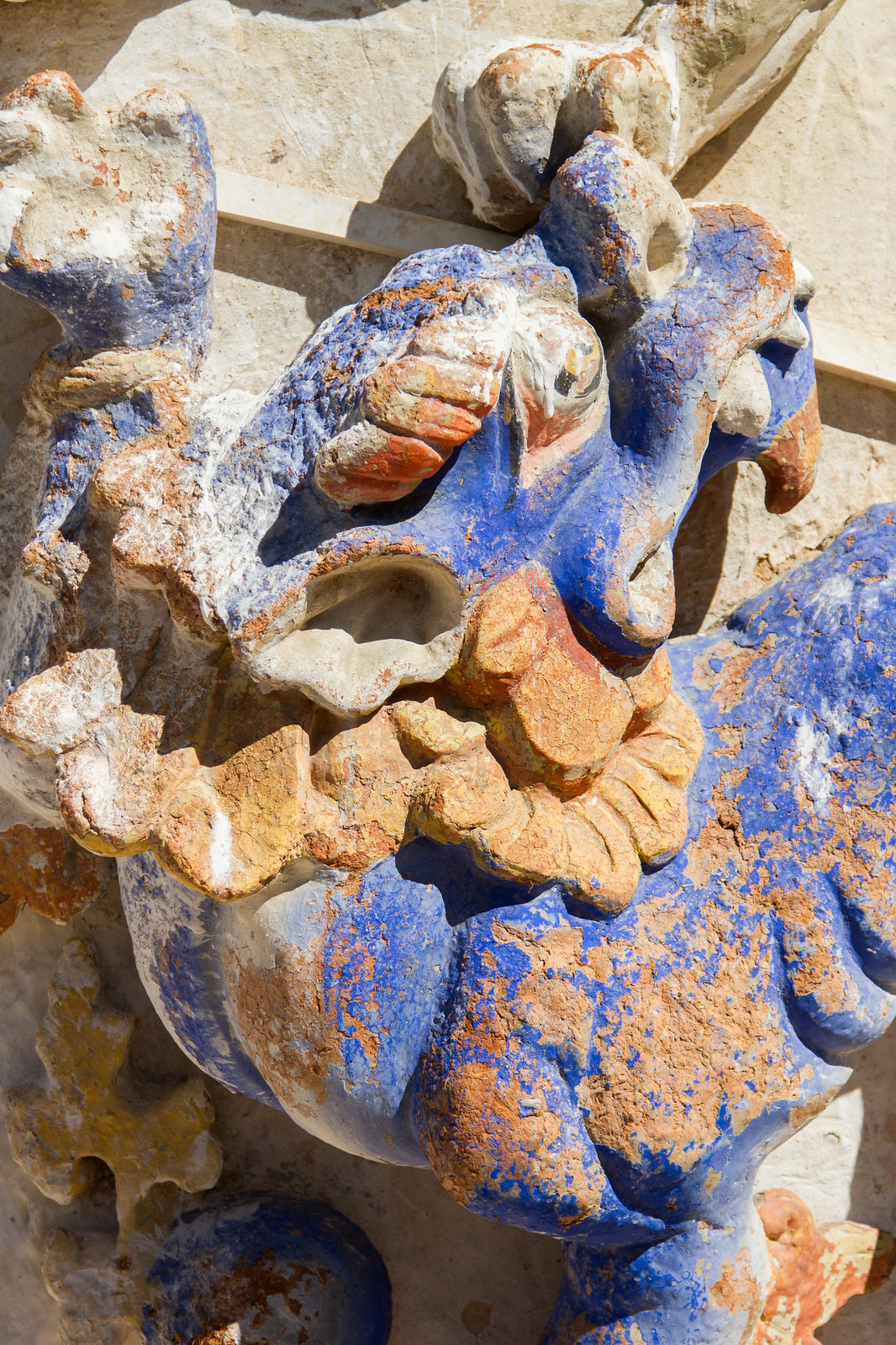 Weathered carved stone dragon relief with faded blue and orange paint on a Tibetan wall.