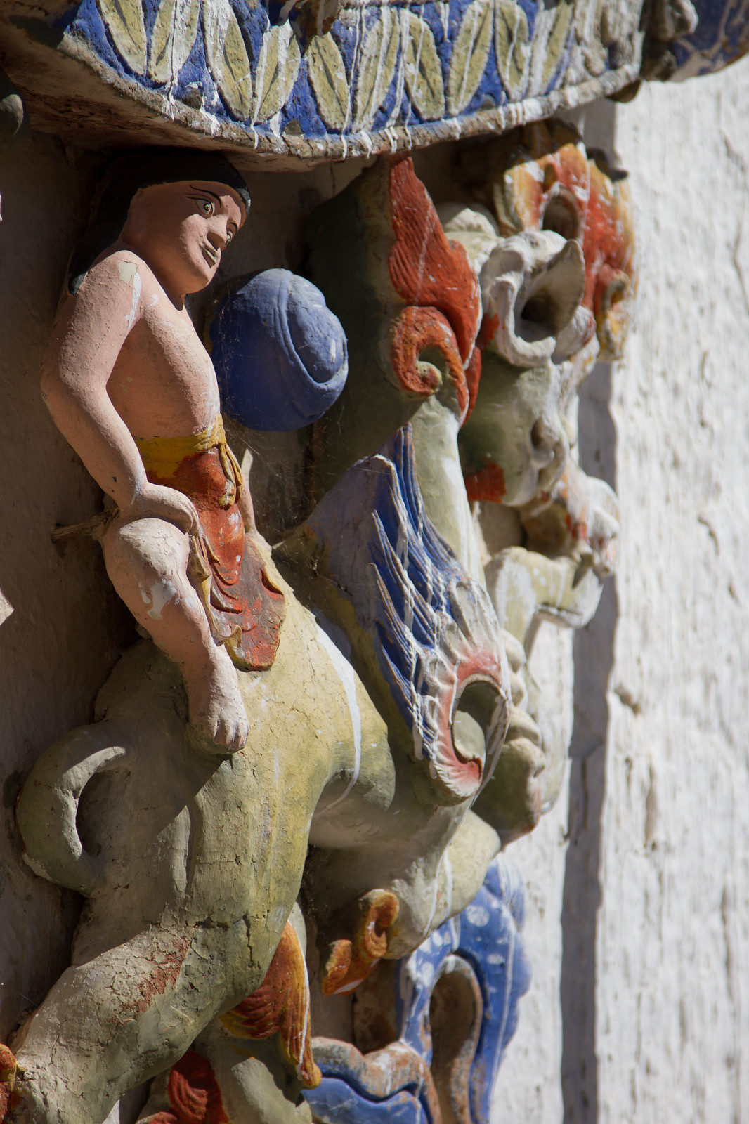 Colorful weathered relief sculptures of a figure and mythical creatures on a Tibetan temple wall.