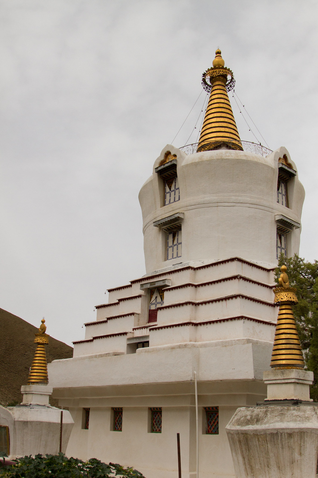 A large whitewashed Tibetan Buddhist stupa with gold spires, flanked by smaller gilded chortens under a hazy sky.