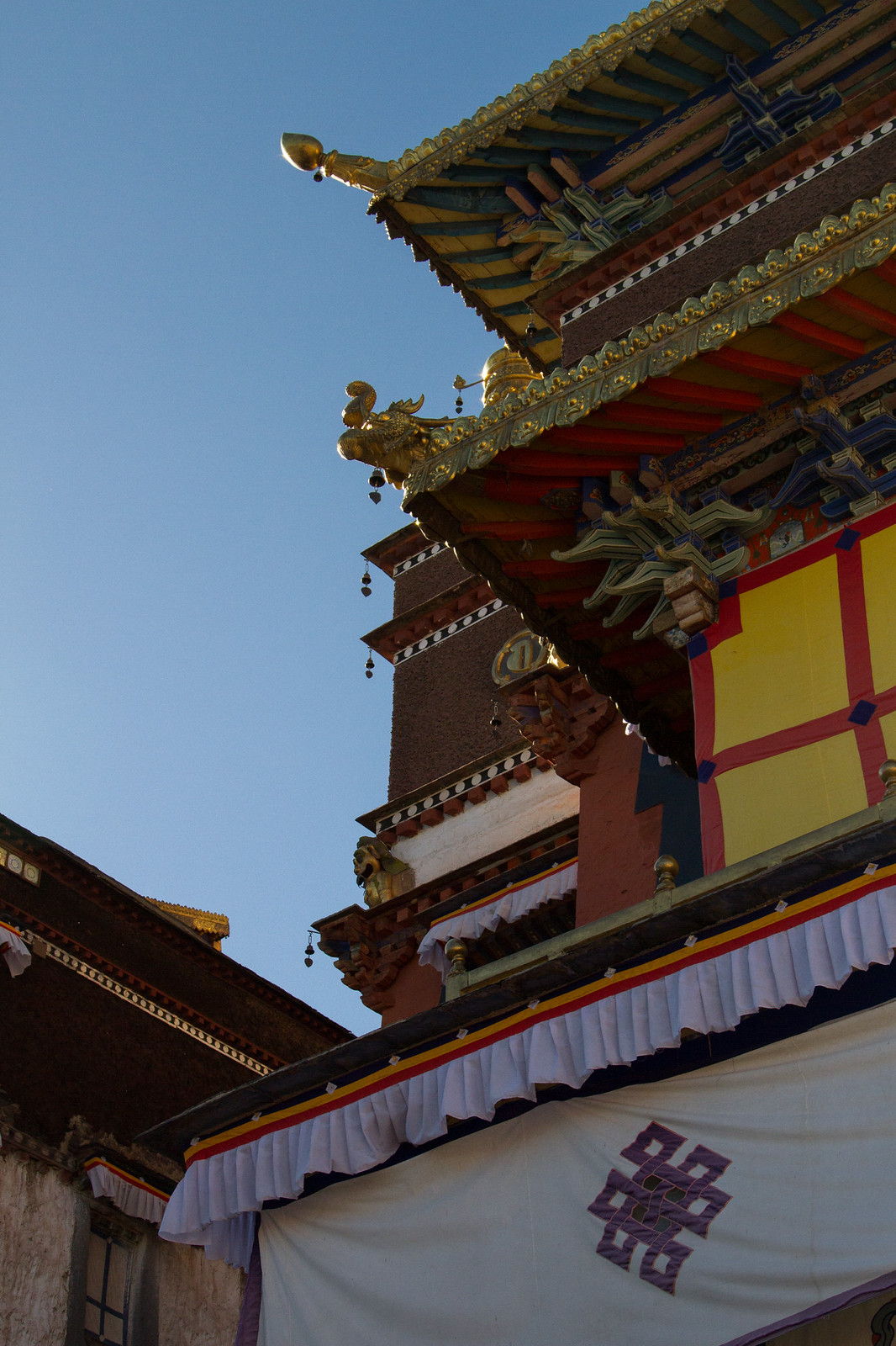 Ornate golden roof of a Tibetan monastery with a dragon finial and endless-knot banner against blue sky.