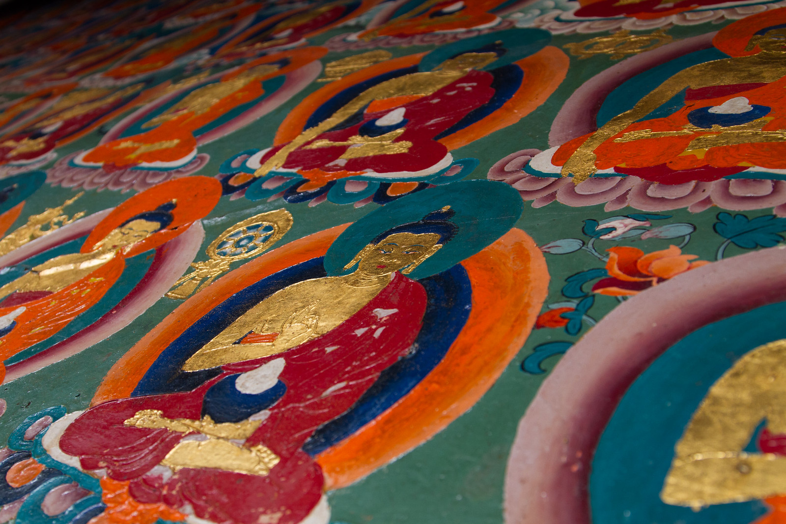 Detail of a Tibetan mural showing rows of gold-bodied seated Buddhas in vivid red, orange, and teal halos.