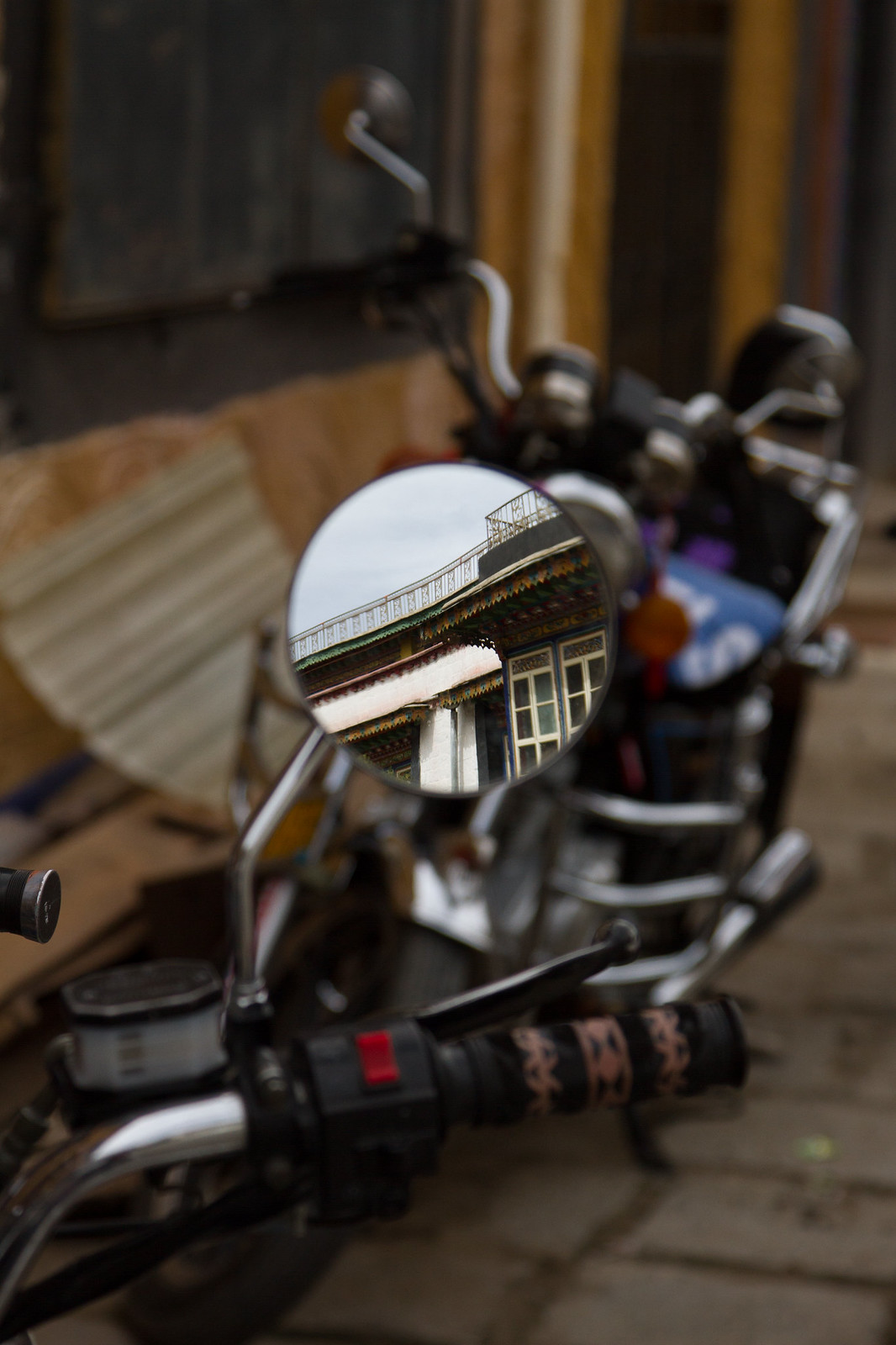 A parked motorcycle's round mirror reflects the ornate green-and-gold eaves of a Tibetan building.