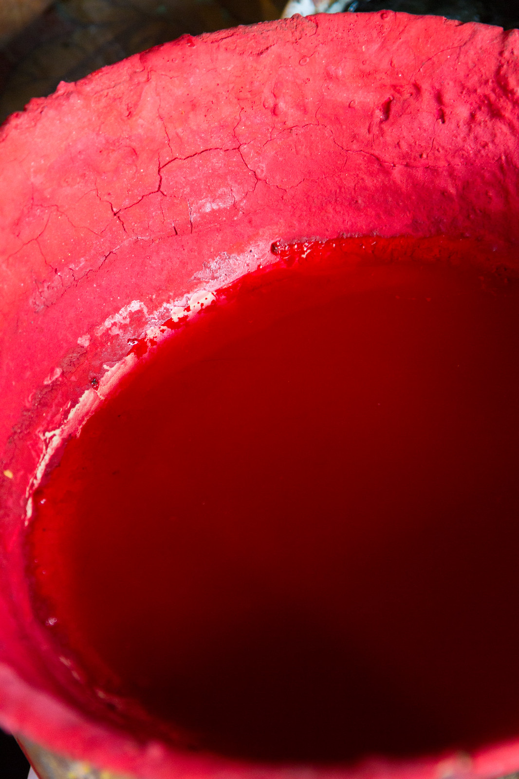 Close-up of a bucket of vivid red pigment powder and paint used to coat Tibetan temple surfaces.