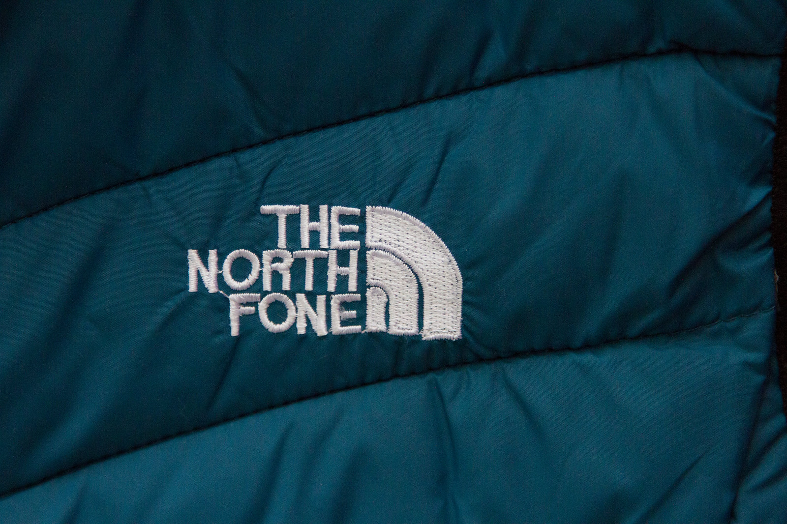 Close-up of a teal puffer jacket with a counterfeit "The North Fone" embroidered logo.