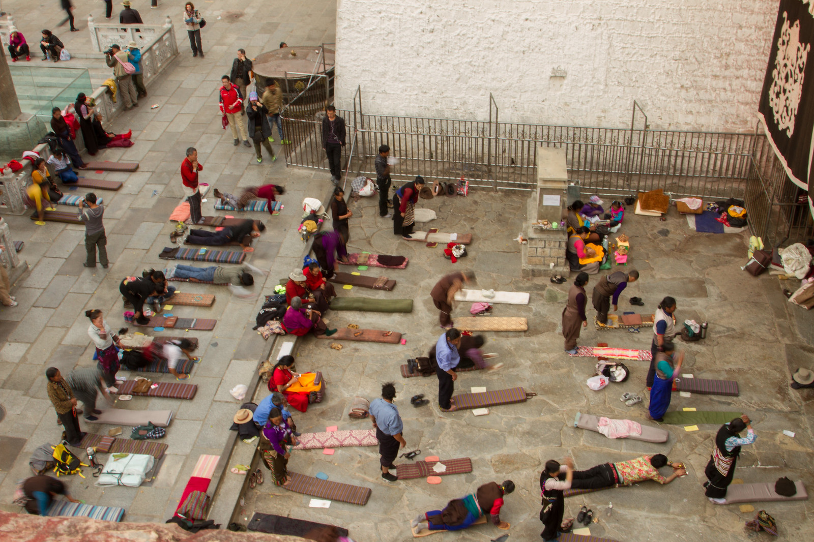 Tibetan pilgrims performing full-body prostrations on mats in a stone plaza outside the Jokhang Temple in Lhasa.