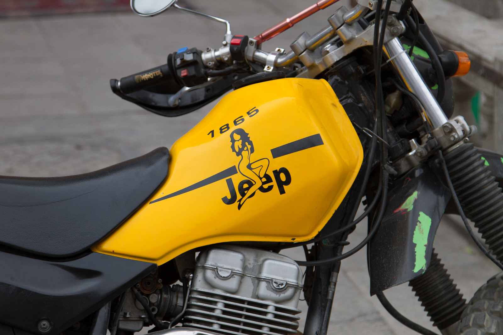Yellow motorcycle fuel tank decorated with "Jeep 1865" and a pin-up figure decal.