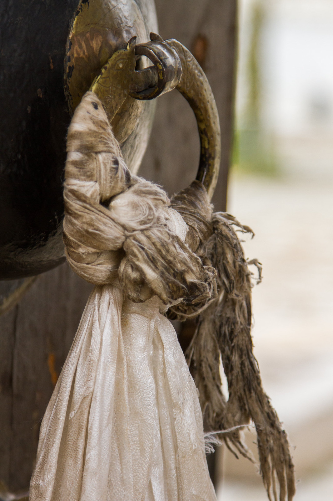 Weathered white khata scarves tied to a brass ring door handle on an old Tibetan door.