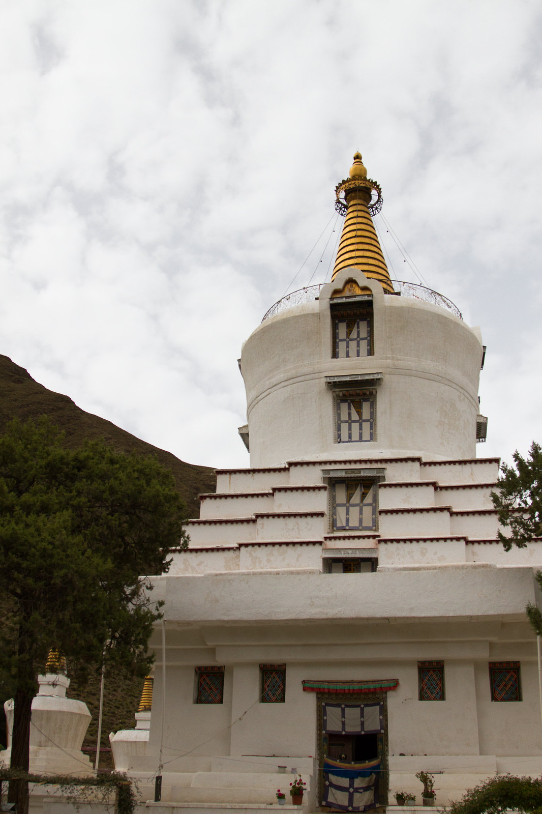 Large white Tibetan stupa with a gold spire and stepped base against a cloudy sky.