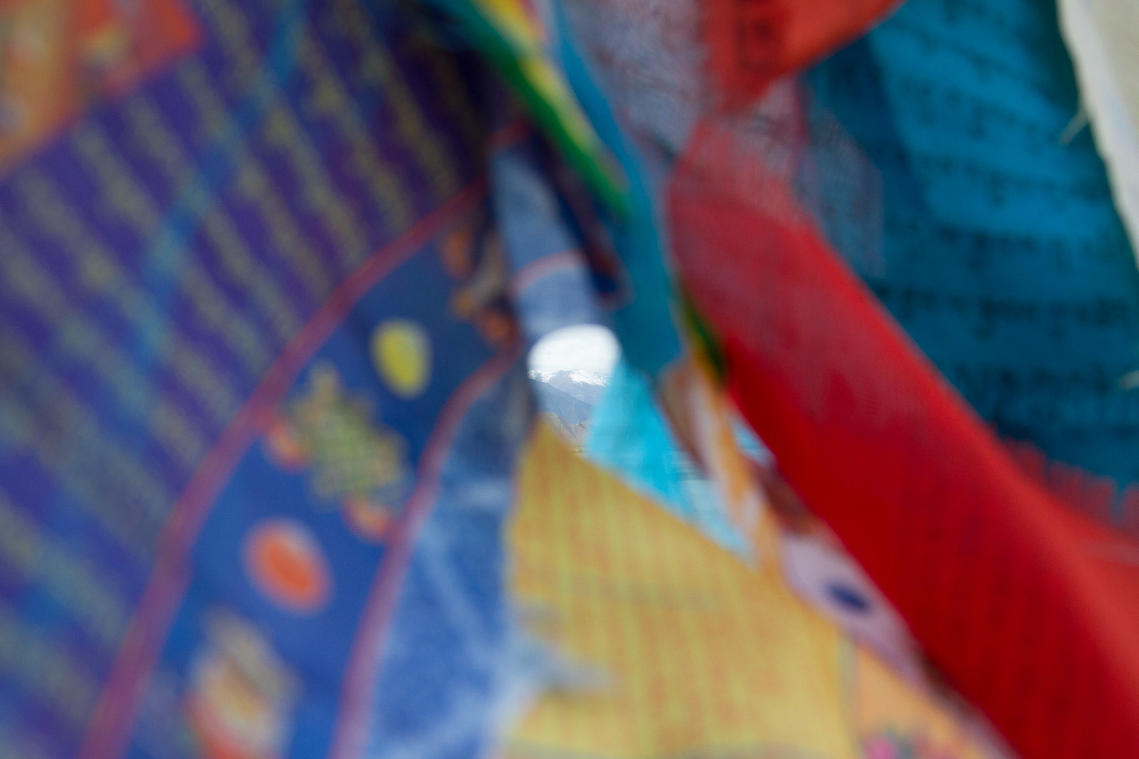 A snow-capped Himalayan peak glimpsed through a close-up flutter of colorful Tibetan prayer flags.