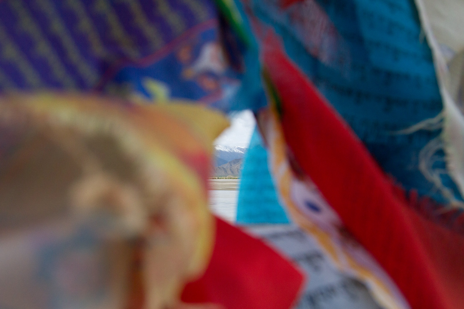 Colorful Tibetan prayer flags framing a distant snow-capped mountain and valley below.