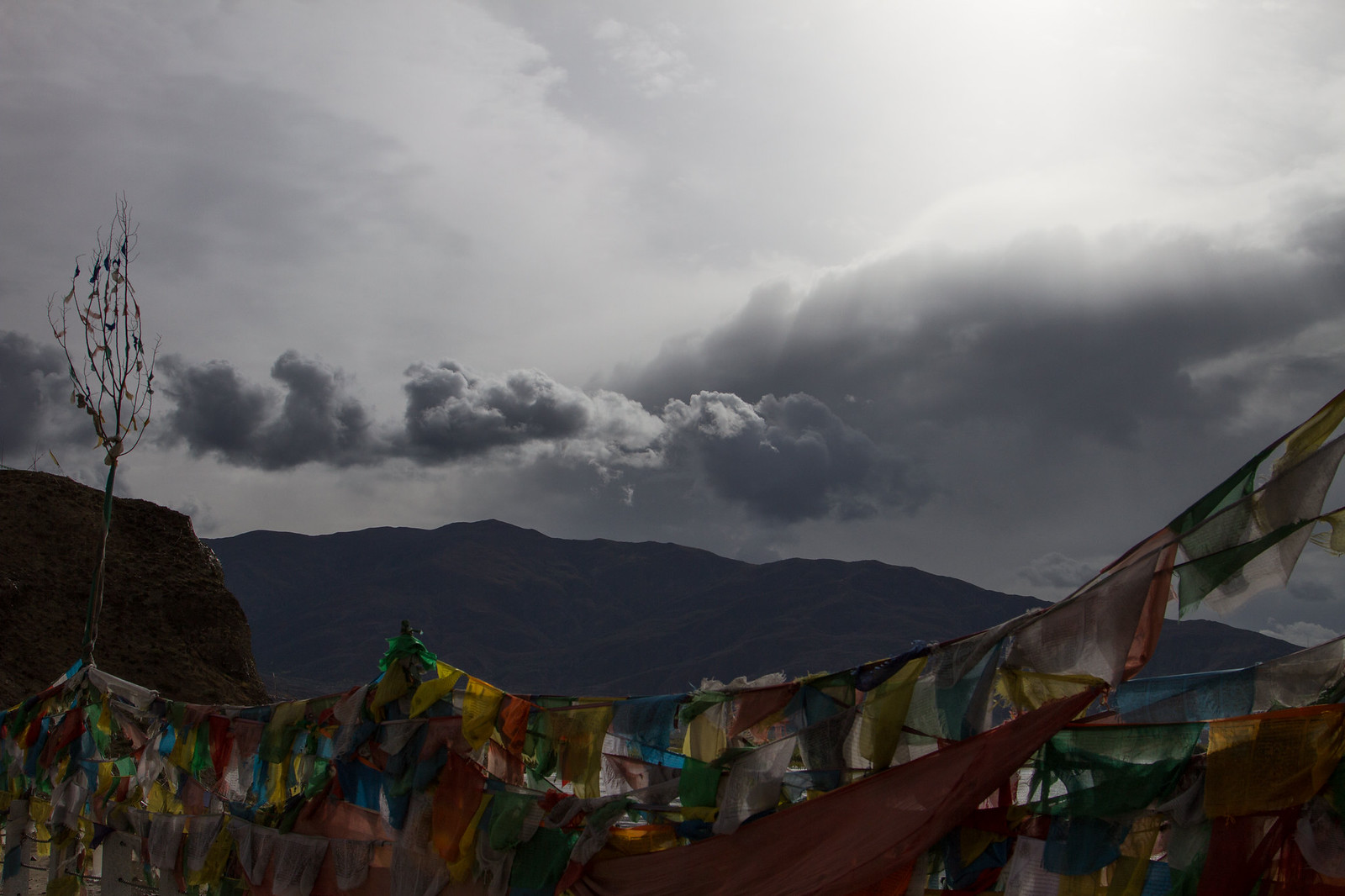 Colorful Tibetan prayer flags strung against dark mountains under a dramatic, cloud-filled sky.
