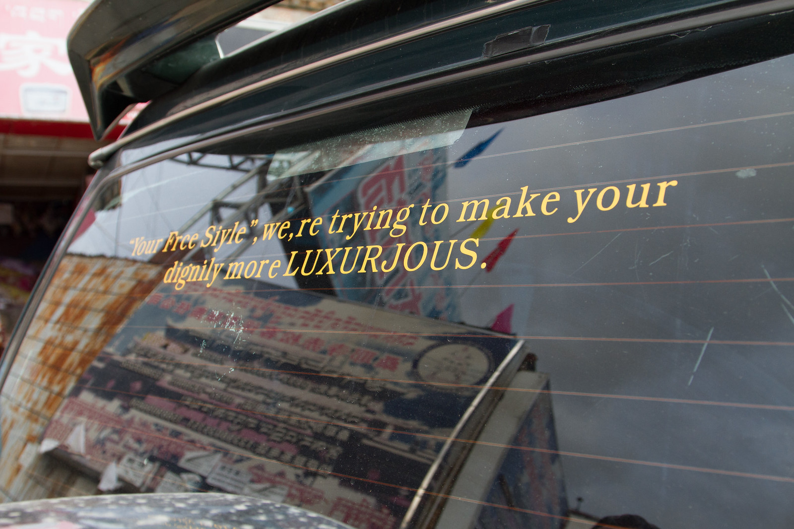Car rear window with garbled gold text: "Your Free Style, we're trying to make your dignity more LUXURJOUS.