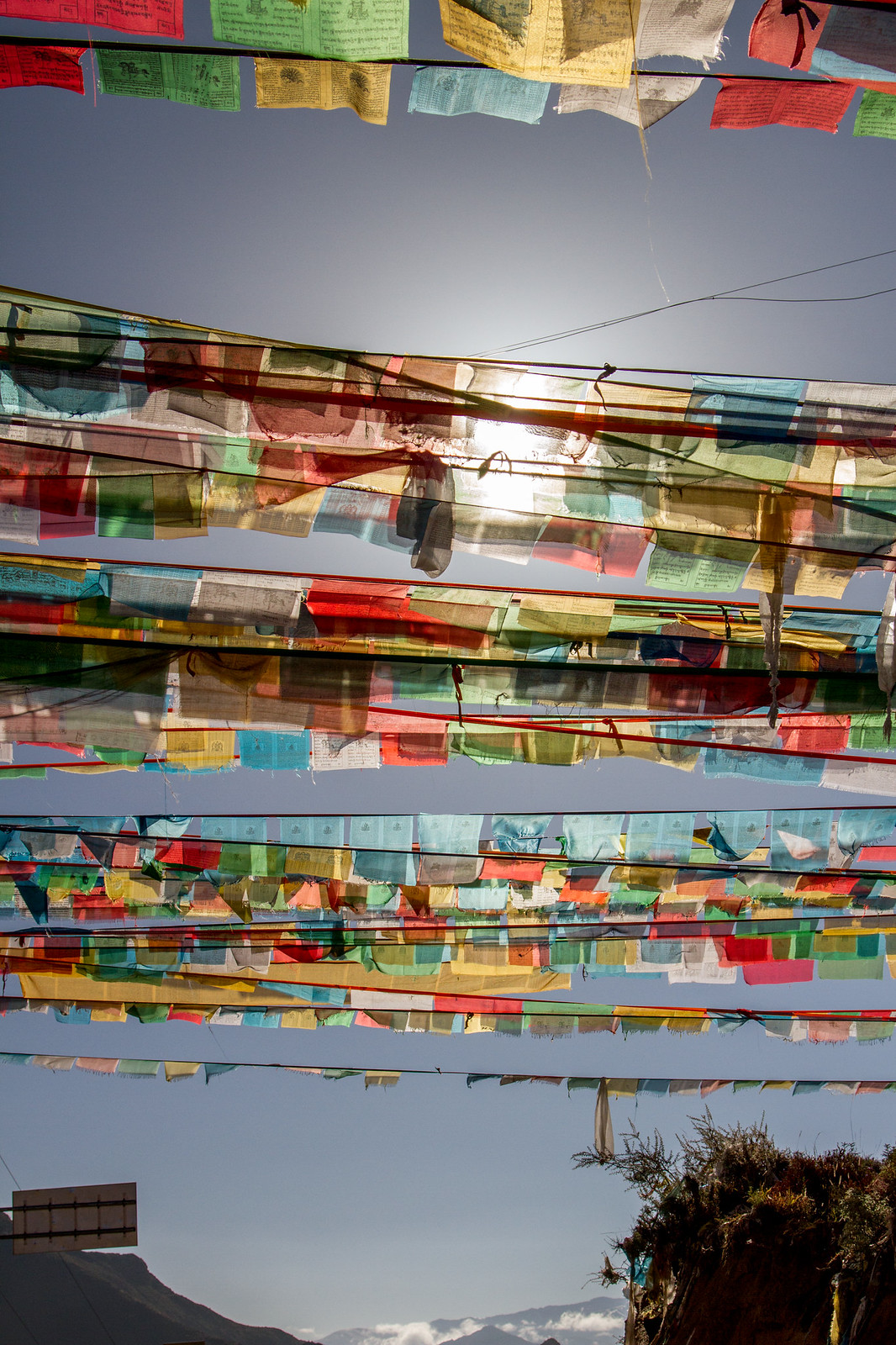 Colorful Tibetan prayer flags strung in rows against a blue sky, backlit by the sun