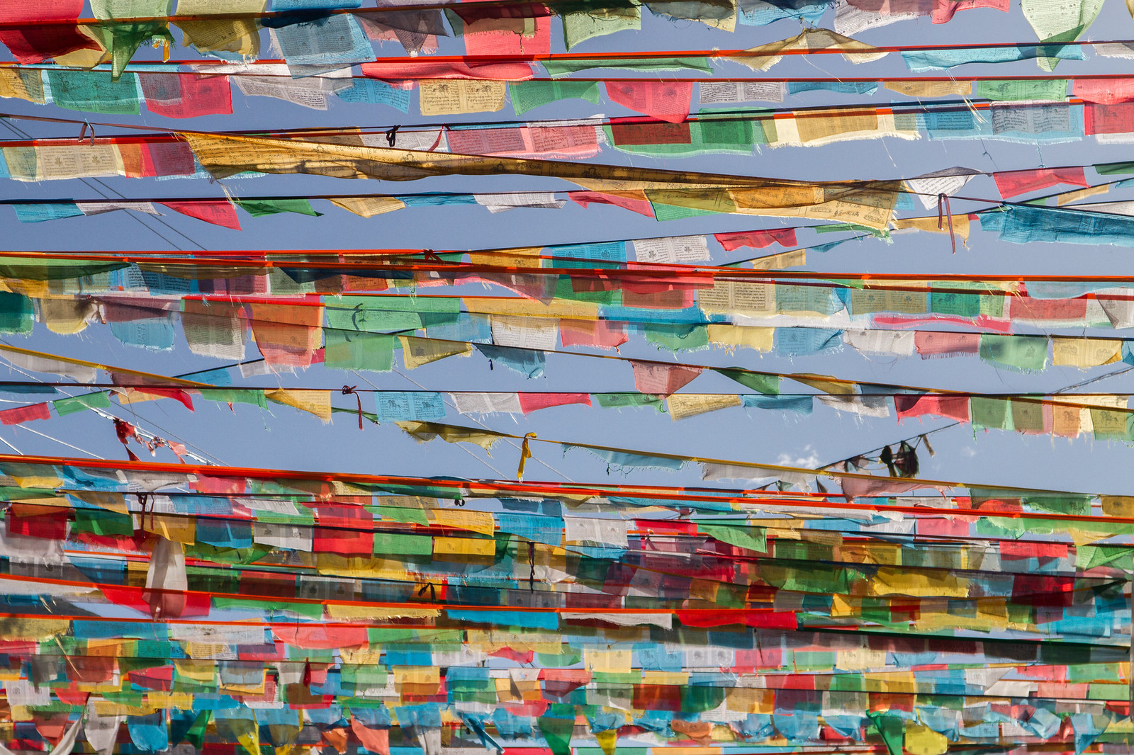 Rows of colorful Tibetan Buddhist prayer flags strung across a clear blue sky.