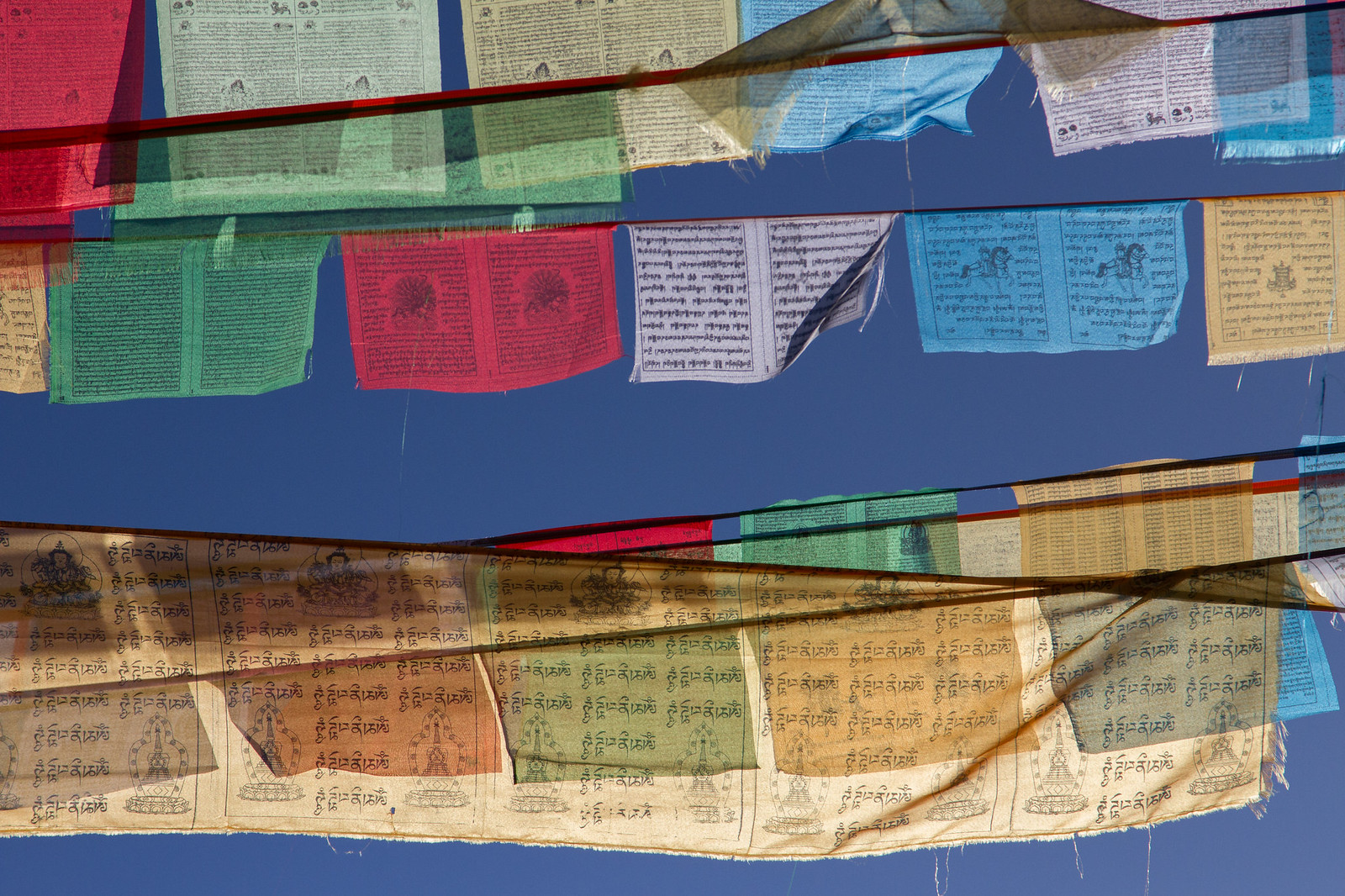 Colorful Tibetan prayer flags printed with scripture and stupa imagery against a deep blue sky.