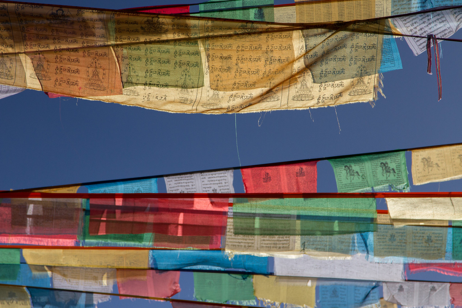 Strings of colorful Tibetan prayer flags printed with mantras and stupas against a deep blue sky.