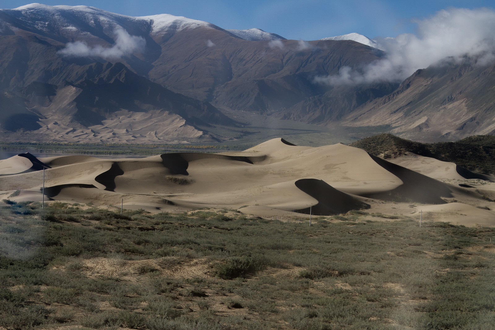 Sculpted sand dunes in a broad valley below snow-capped Himalayan mountains and scattered clouds