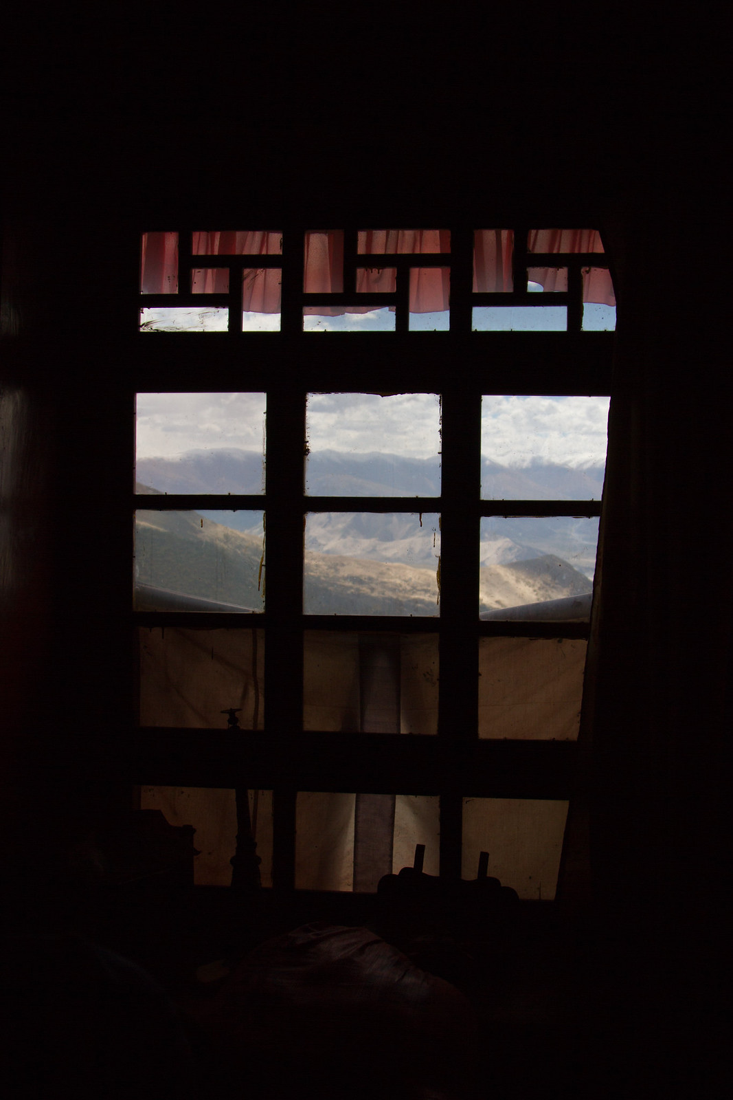 Mountains and clouds seen through a dim latticed window with red curtains