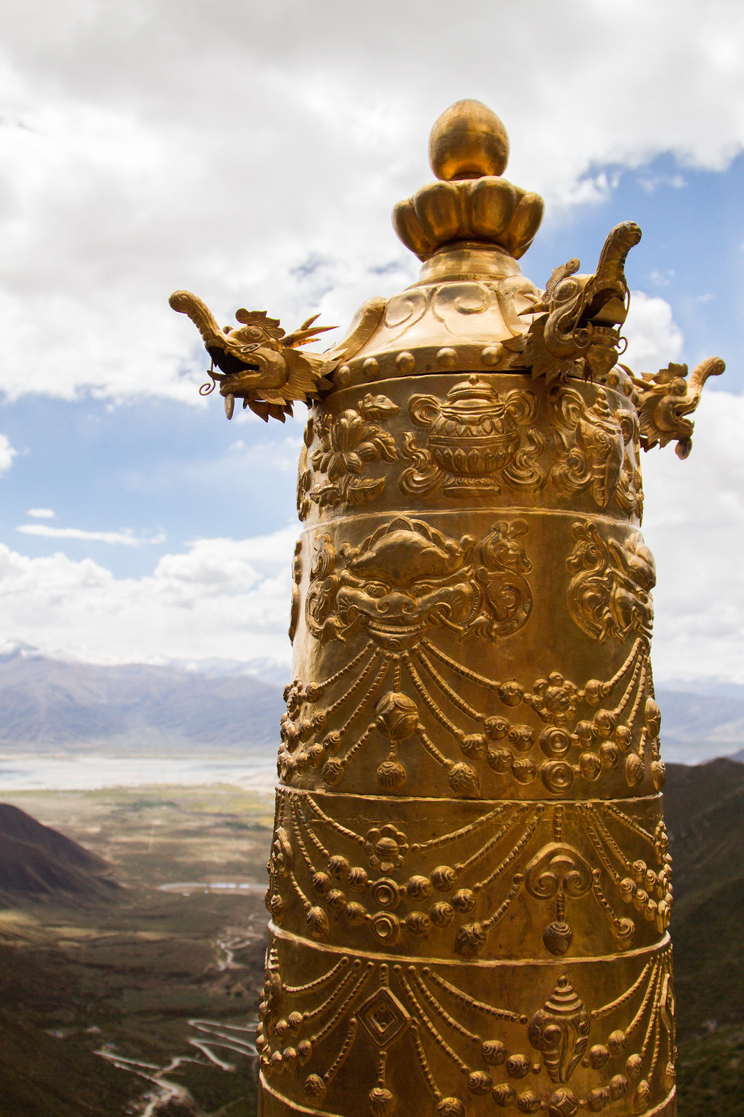 Ornate golden Tibetan rooftop finial with dragon heads, overlooking a valley and distant mountains.