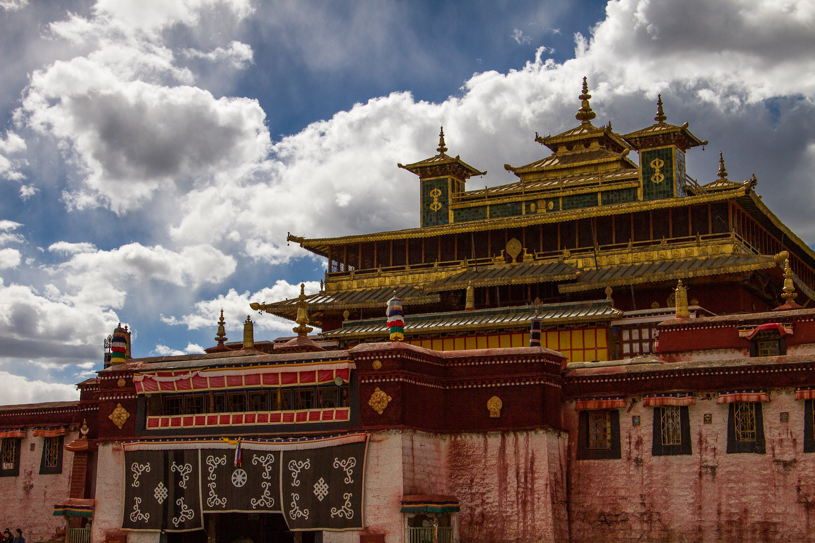 Samye Monastery's golden-roofed main temple with red and white walls under a dramatic cloudy sky, Tibet.