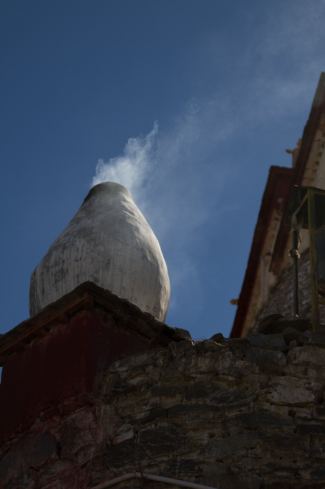 Smoke rising from a whitewashed monastery incense burner against a deep blue Tibetan sky.