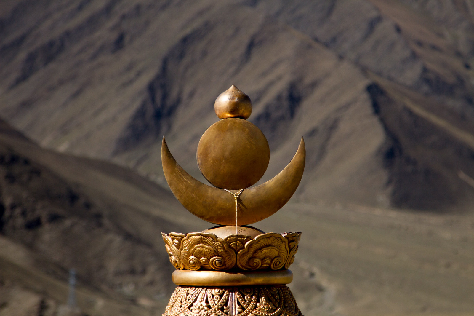 Golden Tibetan sun-and-moon rooftop finial gleaming against a barren mountainside