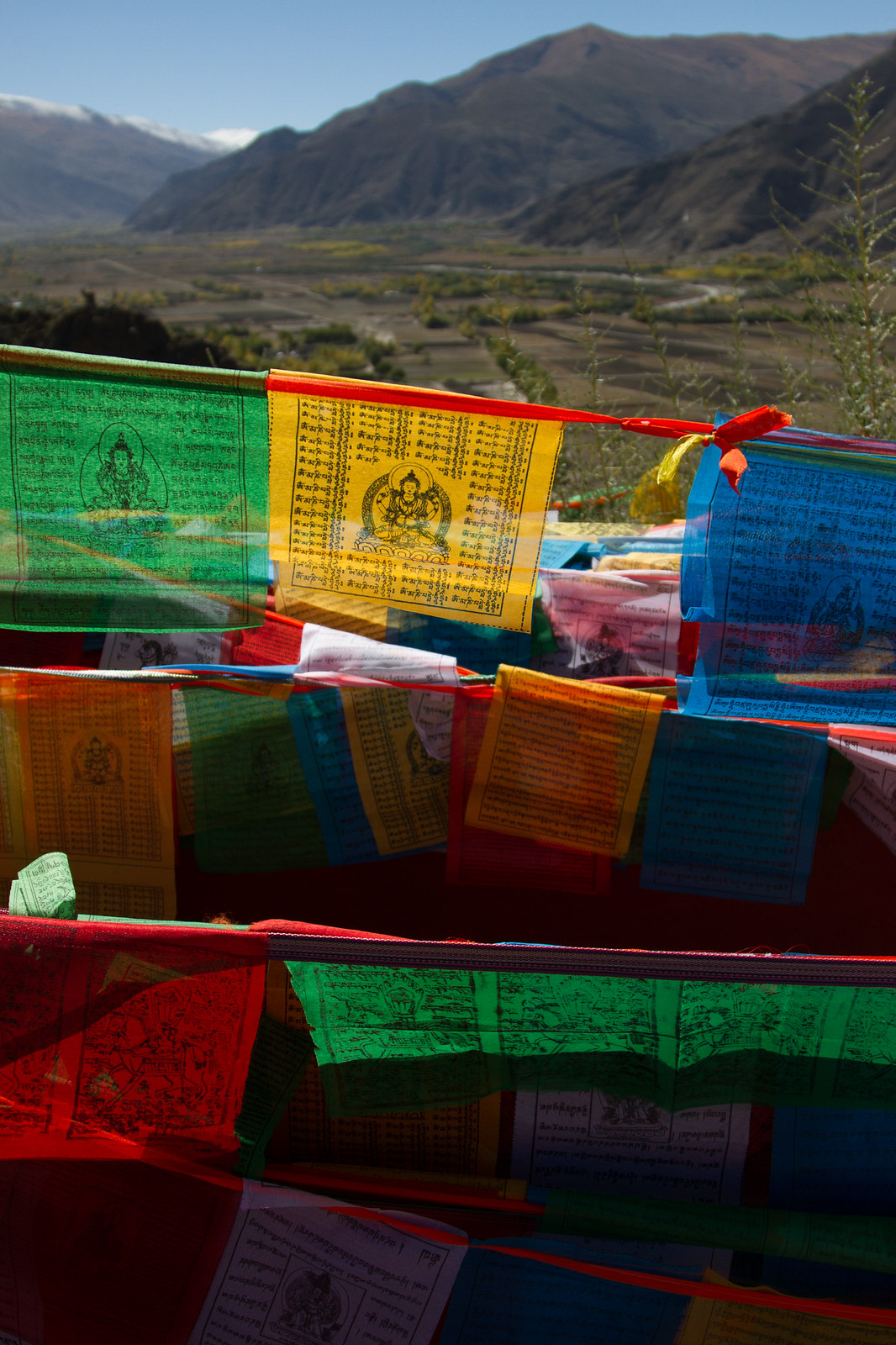 Colorful Tibetan prayer flags printed with scripture and deities strung above a mountain valley.