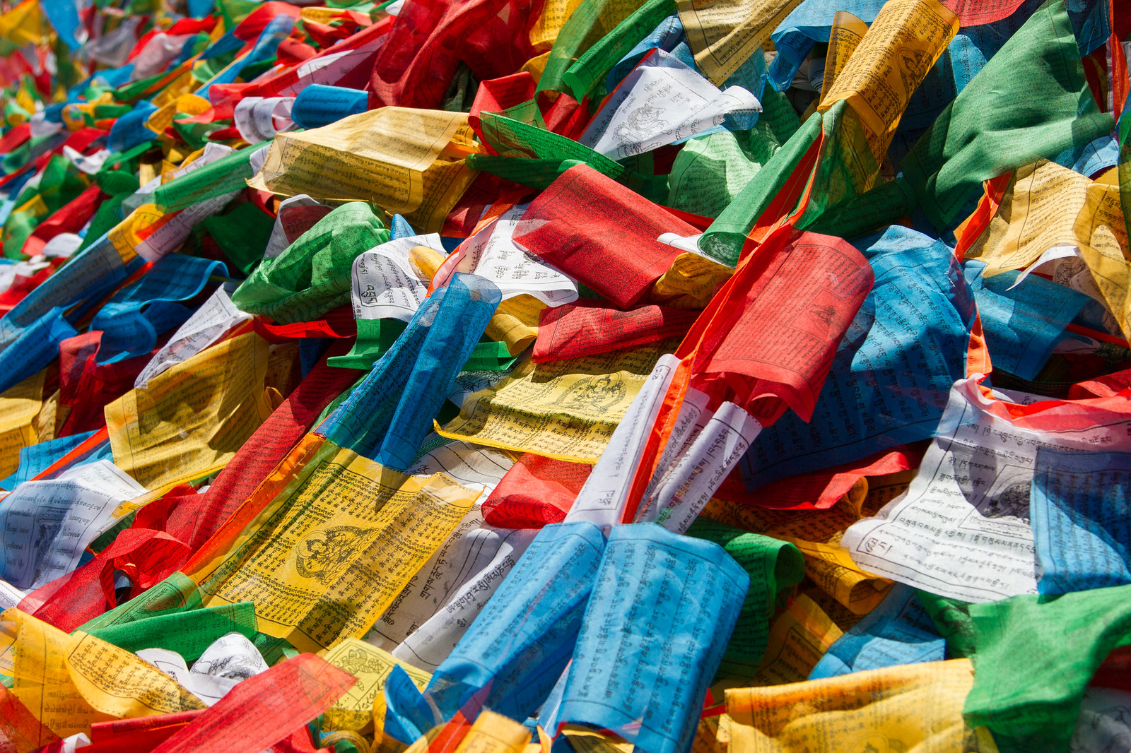 Dense pile of colorful Tibetan prayer flags printed with black Tibetan script and Buddhist figures.