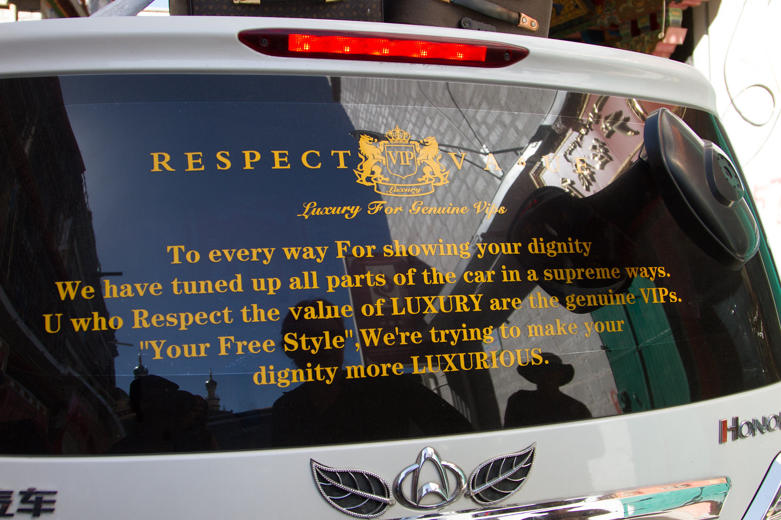 Rear window of a white car with gold "Respect Value — Luxury For Genuine VIPs" decal text