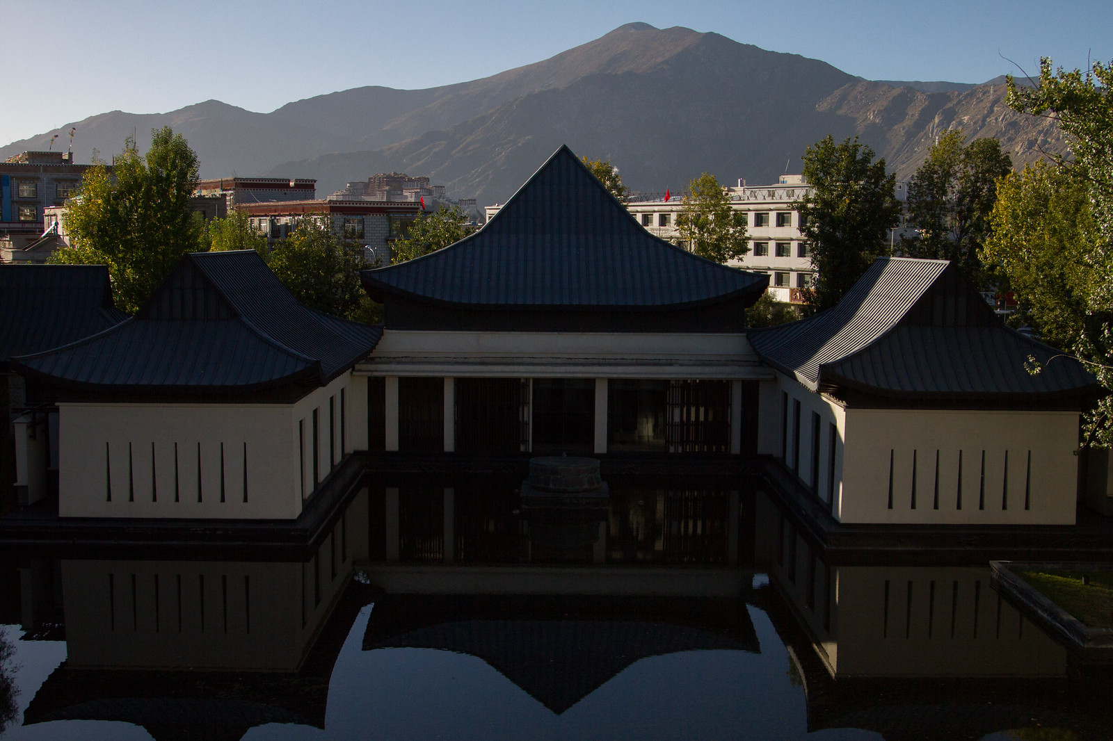 Traditional Tibetan-roofed pavilions mirrored in a still courtyard pool, with a bare mountain rising behind Lhasa.