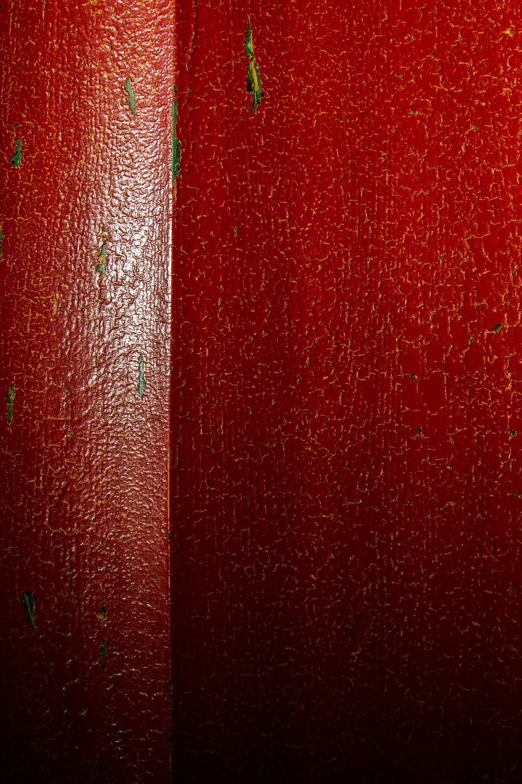 Close-up of weathered, cracked red-painted wood with green undercoat showing through.