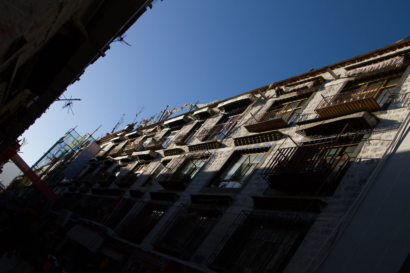 Worm's-eye view of a weathered Tibetan stone building's balconies and windows against a clear blue sky.